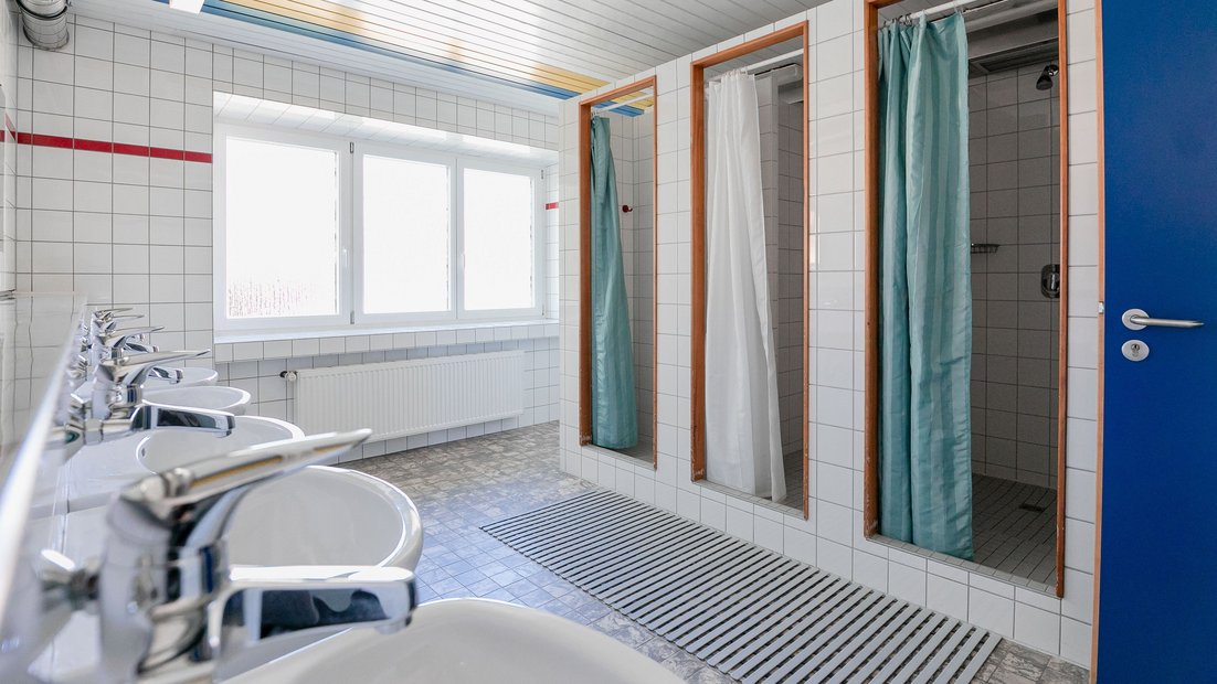 Bagno piastrellato bianco nella casa estiva con più lavandini e docce