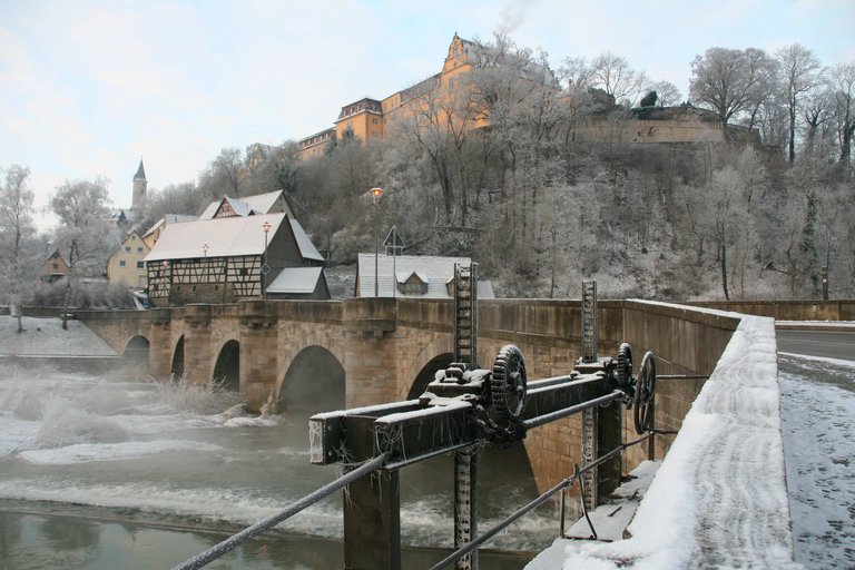 Vista invernale verso il ponte di pietra con archi a tutto sesto e diga sullo Schloss-Berg Kirchberg