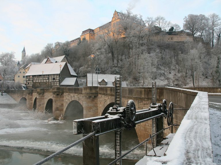 Vista invernale verso il ponte di pietra con archi a tutto sesto e diga sullo Schloss-Berg Kirchberg